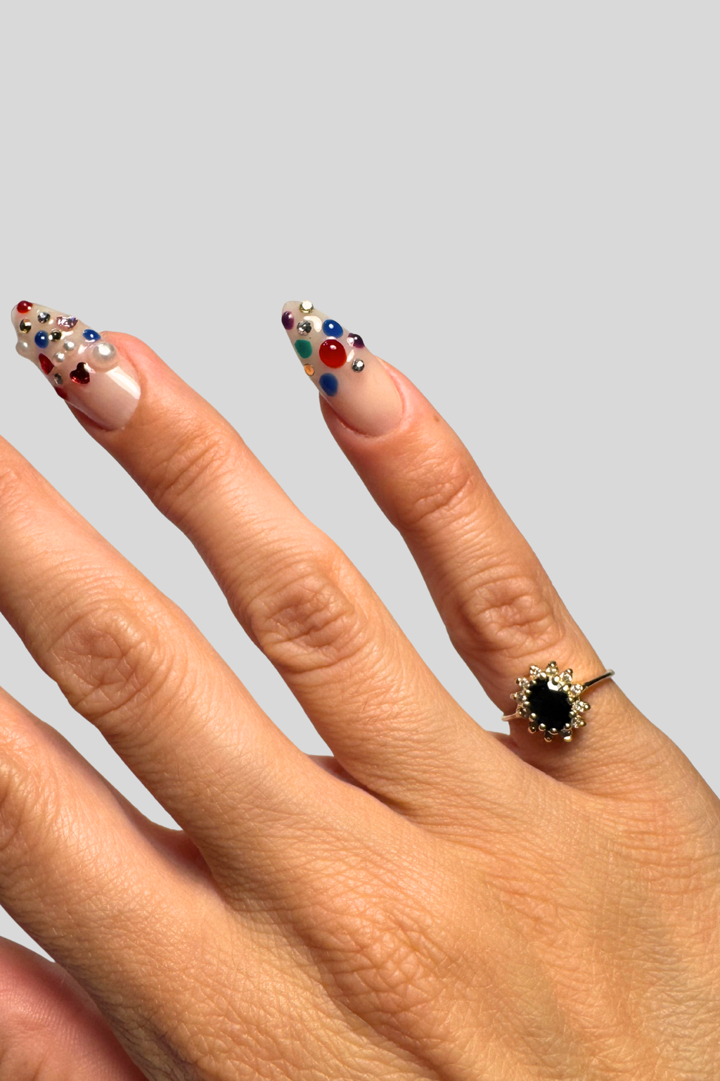 Hand with decorated nails and a ring on a plain background