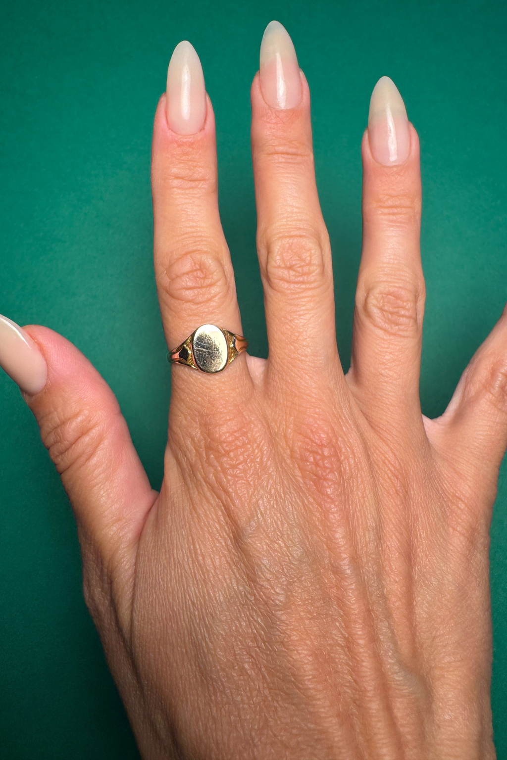 signet ring on female hand with long nails on green background